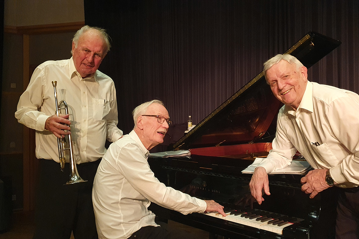 Tre äldre personer vid ett piano.