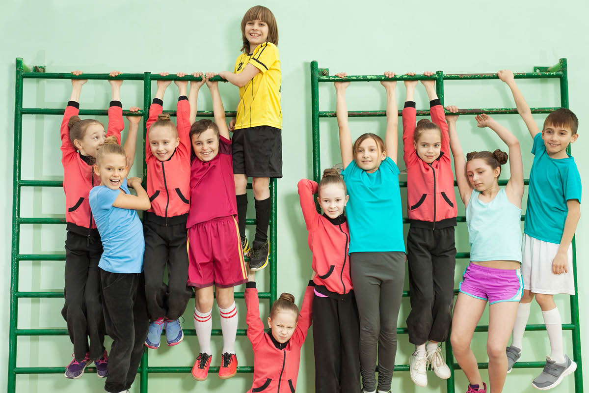 Barn klättrar i ribbstolar i gymnastiksal.