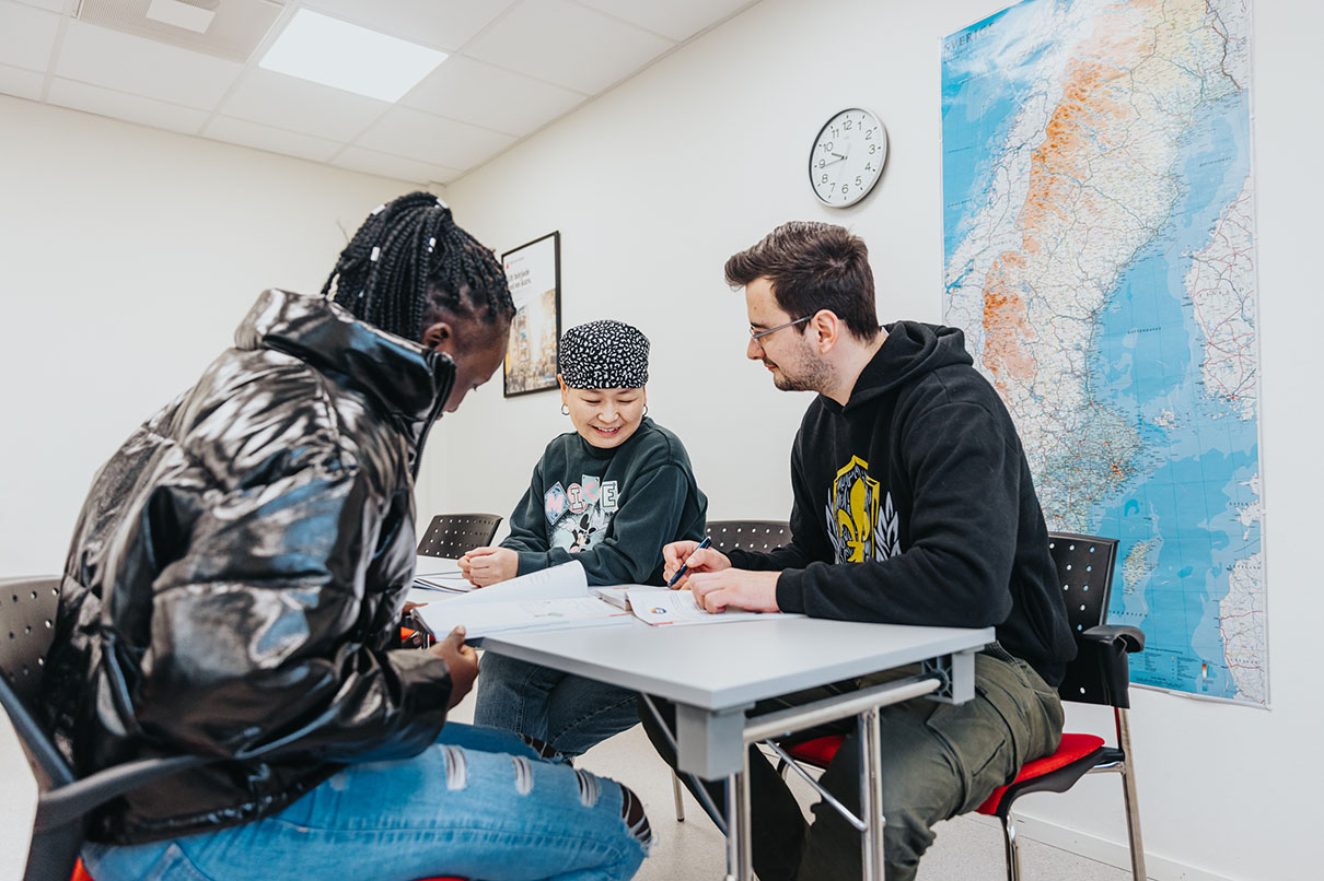 Tre elever sitter och diskuterar i ett klassrum.