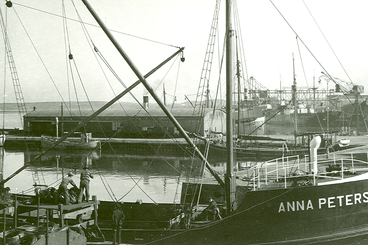 Bild från 30- eller 40-talet från Varbergs hamn. I förgrunden syns en större båt med namnet Anna Peters målat på fören. I bakgrunden skymtar Hoken och den gamla magasinsbyggnaden.