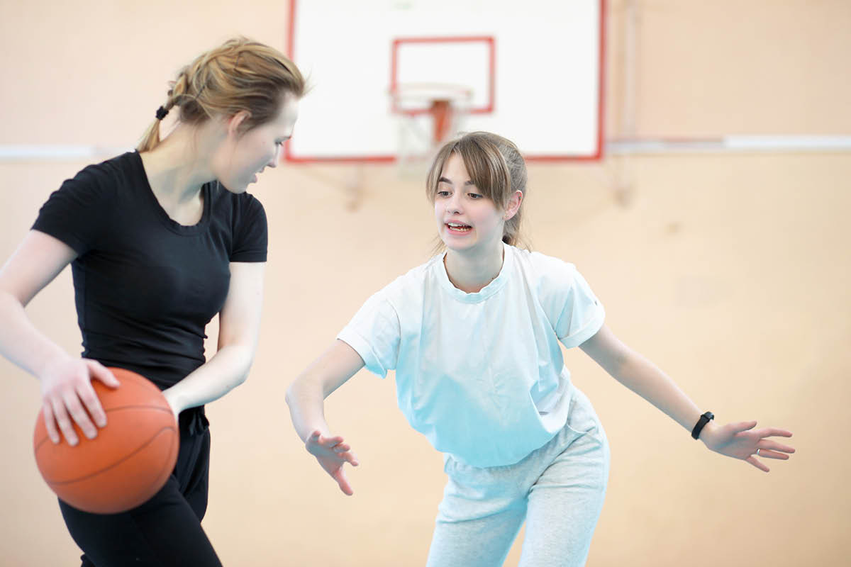 Två tjejer spelar basket i en idrottshall