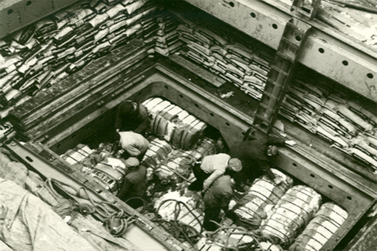 Hamnarbetare lossar bomullsbalar på en båt i hamnen. Historisk bild.