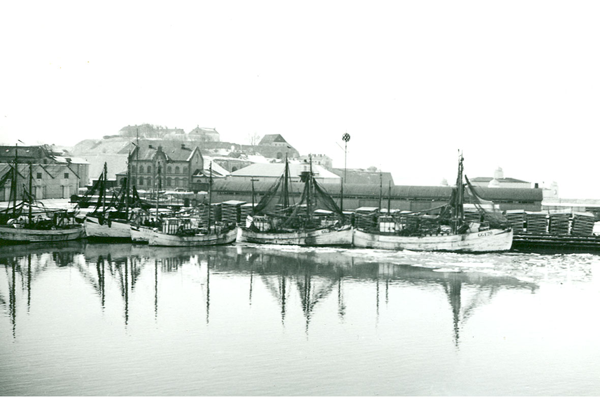 Historisk bild från Varbergs innerhamn. Fiskebåtar och den gamla bågformade varvsbyggnaden på Hoken syns.
