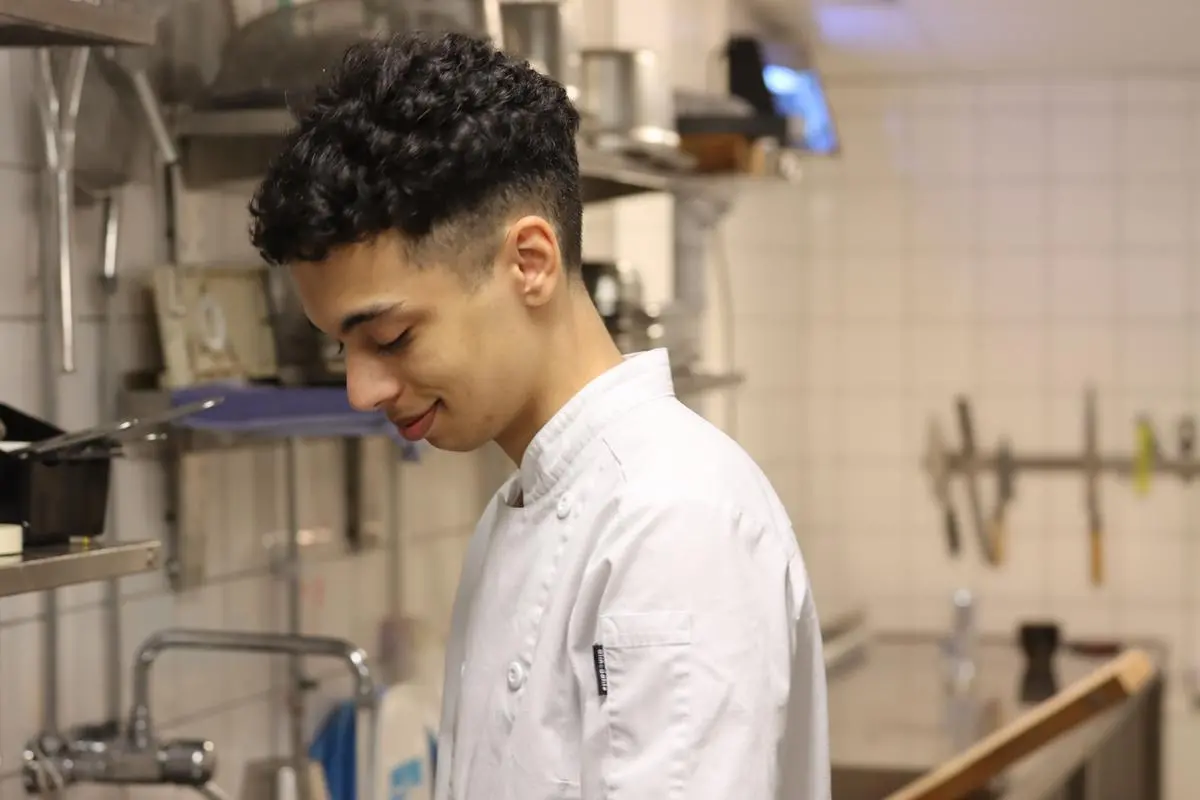 Leende elev iklädd kockkläder står och arbetar i ett kök