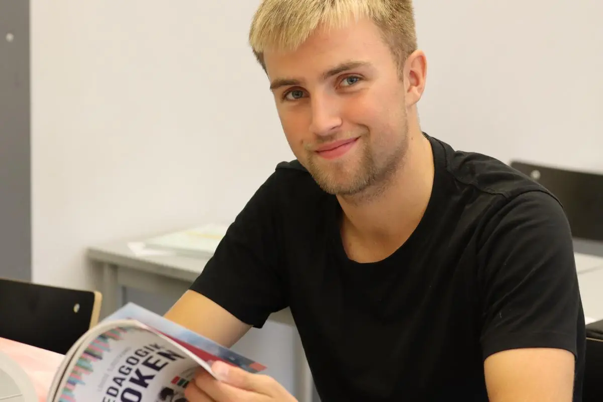 Gymnasieelev håller i en uppslagen bok och tittar leende in i kameran.