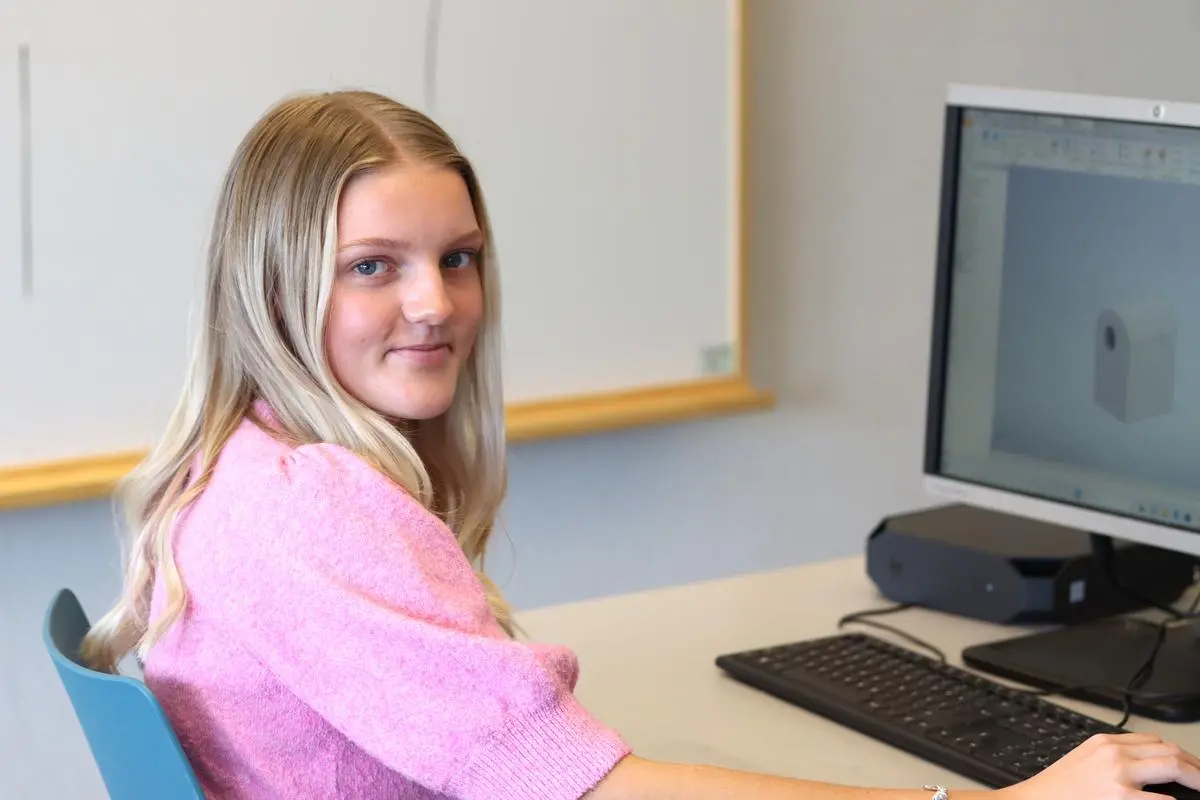 Gymnasieelev tittar mot kameran och sitter framför en dator med ett CAD-program öppet