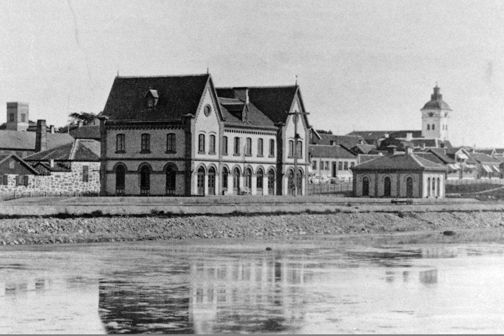 Foto över Varbergs station från 1880-talet med kyrkan i bakgrunden och havet i förgrunden.