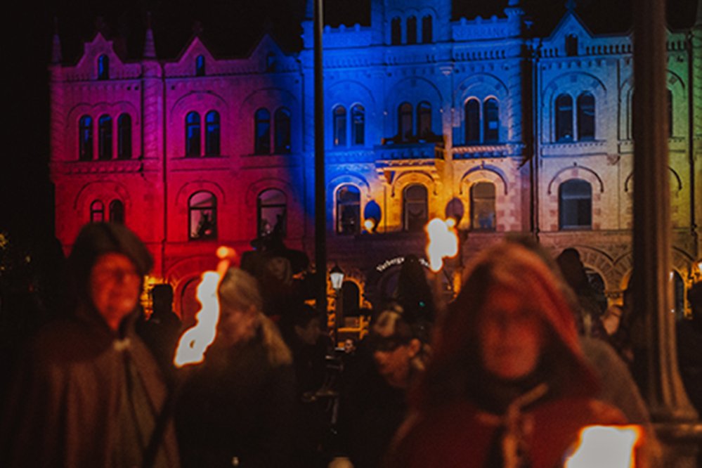 Bild på utklädda människor på torget framför ett upplyst Sparbankshus under eventet Rys och mys en höstkväll.