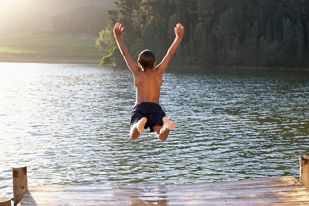 Ryggen på en pojke som hoppar ner i en sjö från en brygga. 